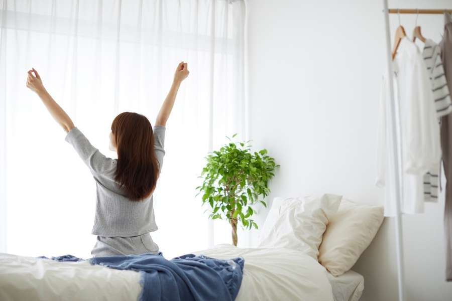 A woman stretching her arms in bed as part of simple morning habits.