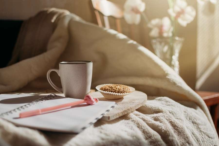 A warm cup of coffee and a notebook on a bed setup, highlighting a peaceful sustainable morning routine.