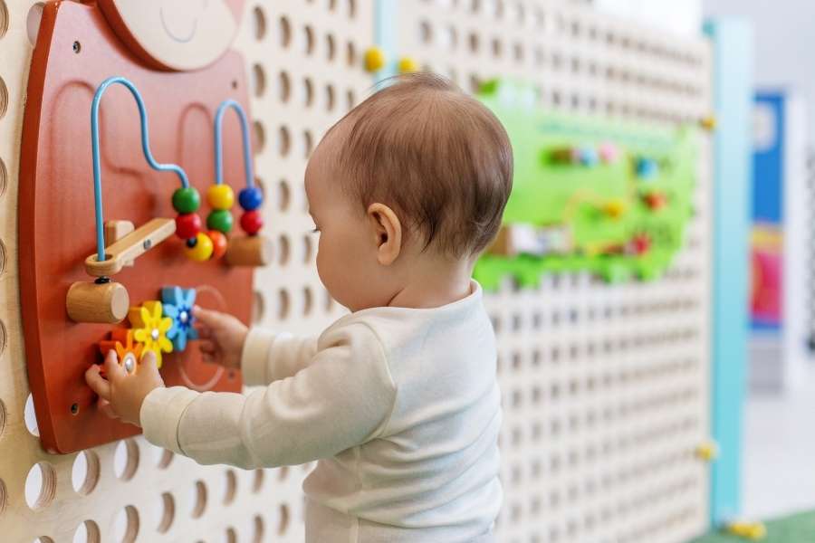 A baby playing with a colourful wall activity board during potent training.